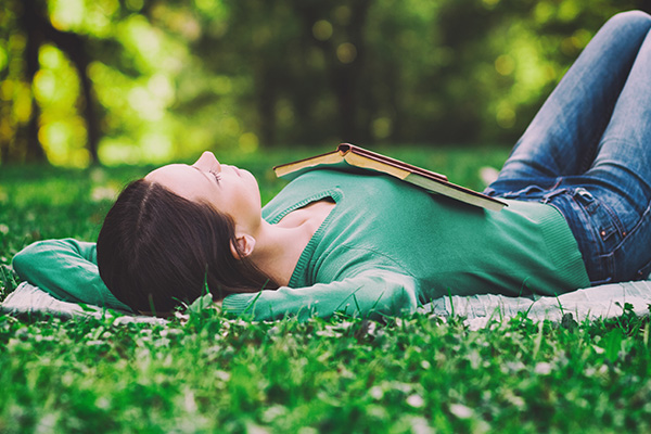 Woman laying on blanket in the grass with a book open. 