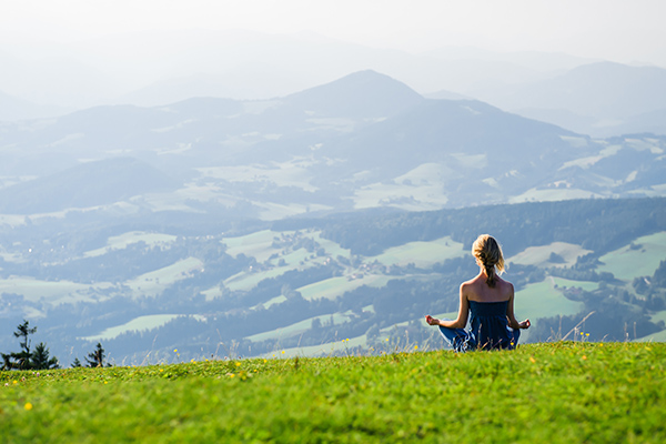 Woman meditating on a hilltop with a gorgeous mountain view. 