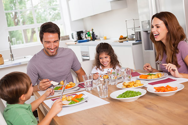 Family of four eating dinner together at the kitchen table having a fun conversation. 